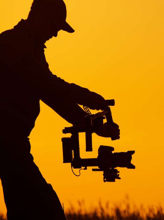 Video Stabilizer Operator. Taking Video Shoots Using DSLR Gimbal Equipment. Sunset Silhouette Concept.